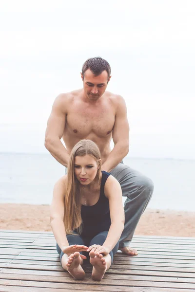Hamile kadın ve erkek kumsalda yoga yapıyorsun — Stok fotoğraf