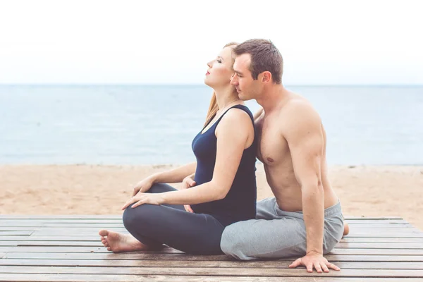 Mann und schwangere Frau machen Yoga am Strand — Stockfoto