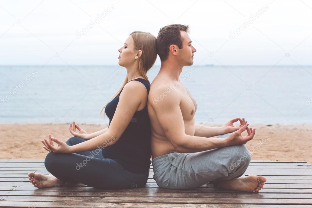 Man and pregnant woman are doing yoga on the beach