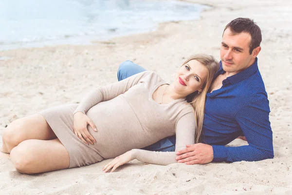 Man och gravid kvinna vilar på stranden — Stockfoto