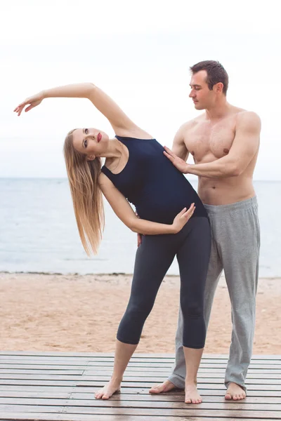 Hamile kadın ve erkek kumsalda yoga yapıyorsun — Stok fotoğraf