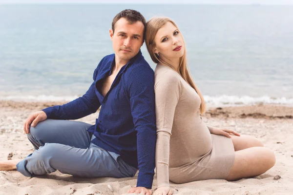Uomo e donna incinta riposano sulla spiaggia Foto Stock Royalty Free