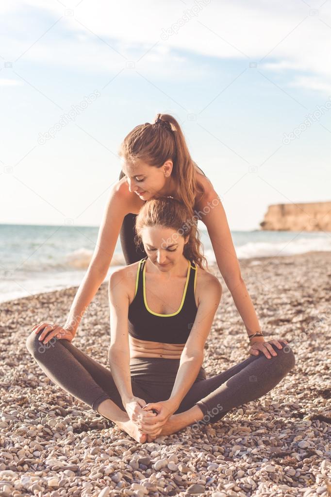Two girls are doing stretching on the beach