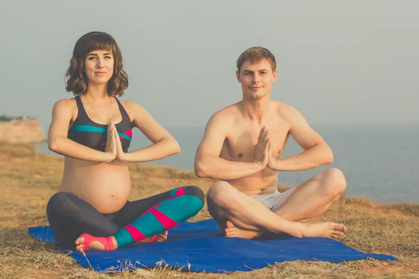 Hombre y esposa embarazada están haciendo yoga en la playa —  Fotos de Stock