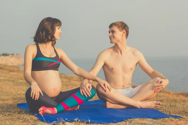 Man and pregnant wife are doing yoga on the beach — Stock Photo, Image
