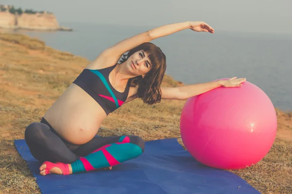 Беременная девочка с розовым мячом делает растяжку — стоковое фото