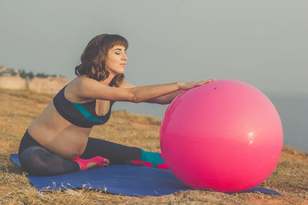 Embarazada chica con rosa fitball haciendo estiramiento —  Fotos de Stock