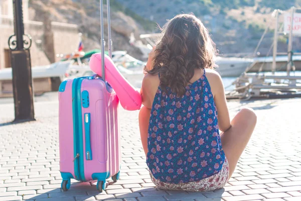 Девушка сидит с розовым чемоданом — стоковое фото