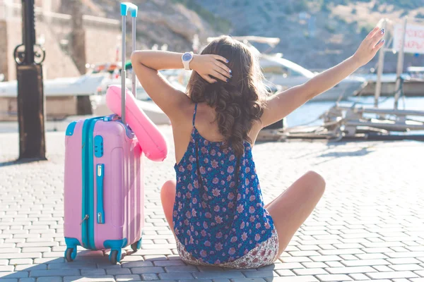 Viajante menina está sentada com mala rosa — Fotografia de Stock