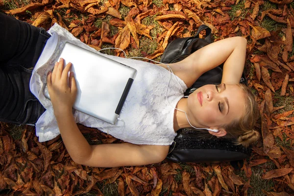 Menina adolescente com tablet digital deitado no parque de outono — Fotografia de Stock