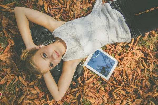 Menina adolescente com tablet digital deitado em folhas — Fotografia de Stock