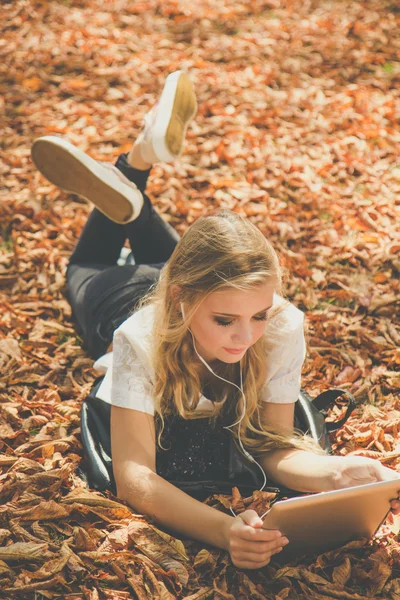 Menina adolescente com tablet digital deitado em folhas — Fotografia de Stock