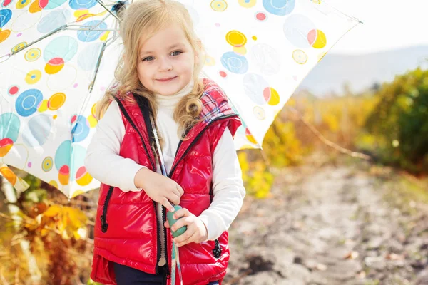 Little girl with umbrella in red vest outdoor