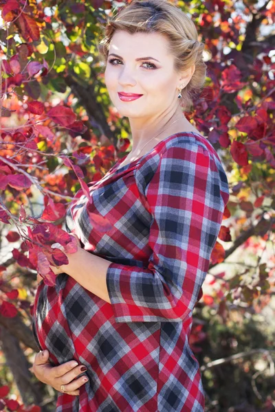 Pregnant girl is wearing checkered dress in park — Stock Photo, Image