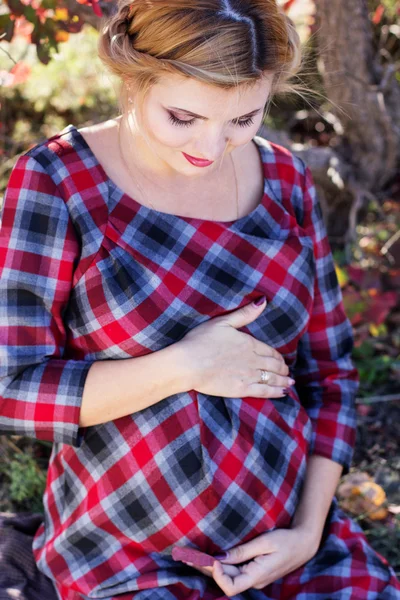 Těhotná dívka má na sobě kostkované šaty v parku — Stock fotografie
