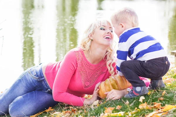 Madre e hijo cerca del lago con calabaza, otoño — Foto de Stock