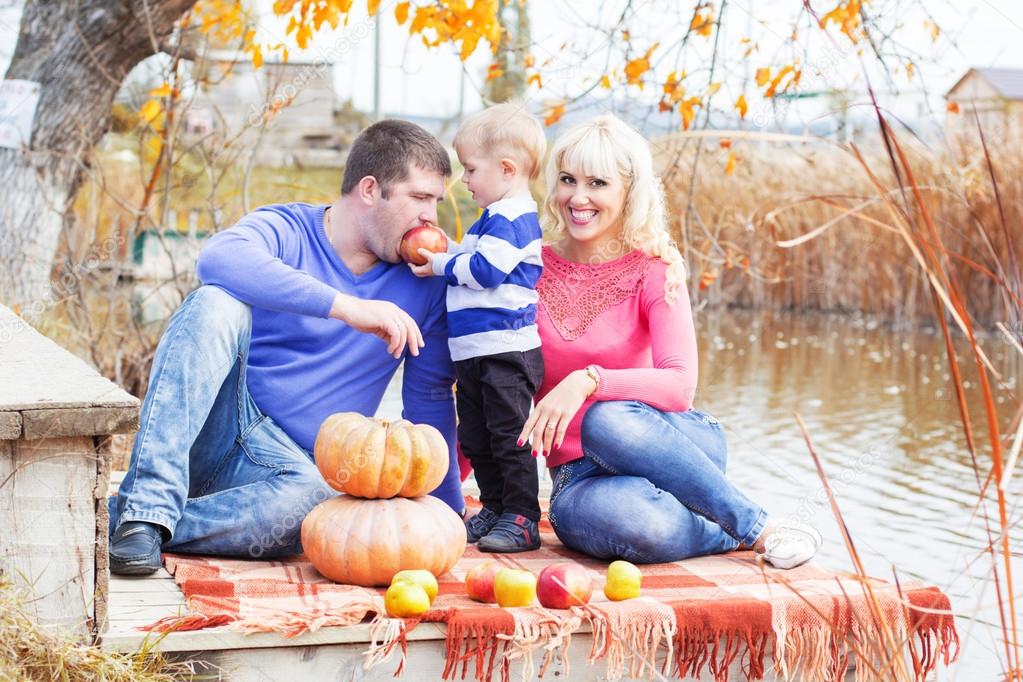 Young family near lake with pumpkins, autumn time