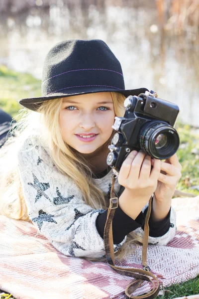 Cute little girl is resting near lake with camera — Stock Photo, Image