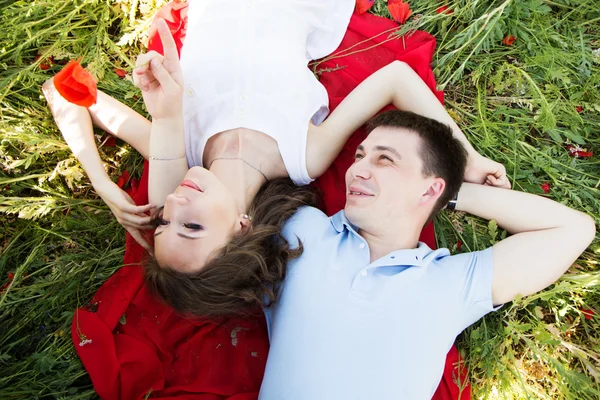 Casal deitado em um prado cheio de papoilas — Fotografia de Stock