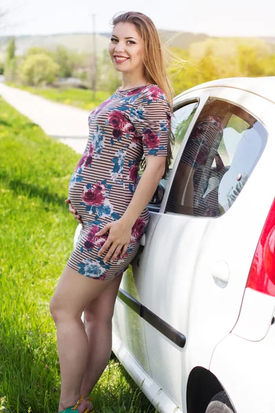 Счастливая беременная женщина стоит рядом с белой машиной — стоковое фото
