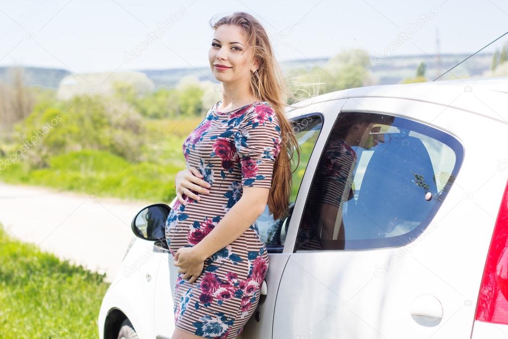 Happy pregnant woman standing near car