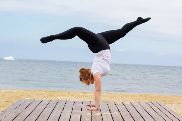 Sportig knubbig kvinna gör handstand nära havet — Stockfoto