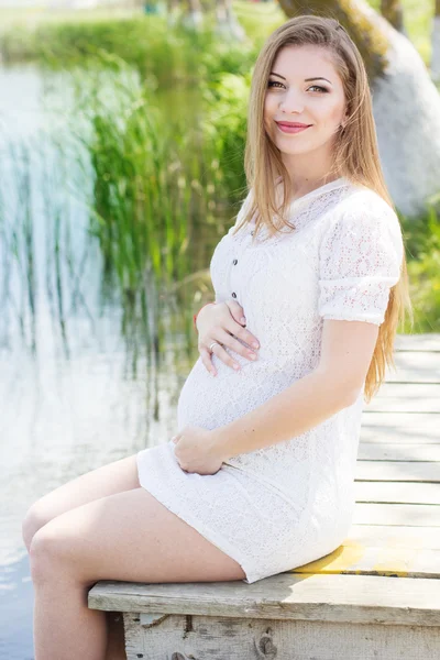 Беременная девушка сидит на мосту у реки — стоковое фото
