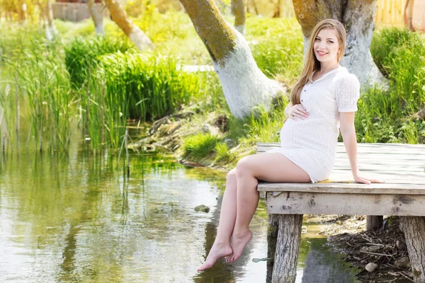 Glad gravid kvinna sitter nära floden — Stockfoto