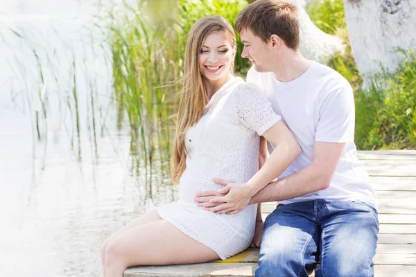 Zwangere vrouw met echtgenoot zitten op brug — Stockfoto