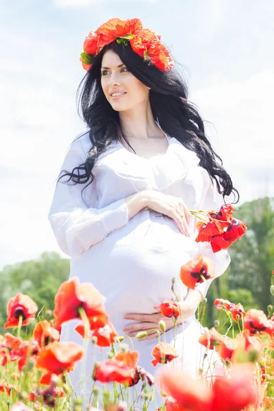Happy pregnant brunette girl on poppy field — Stok Foto