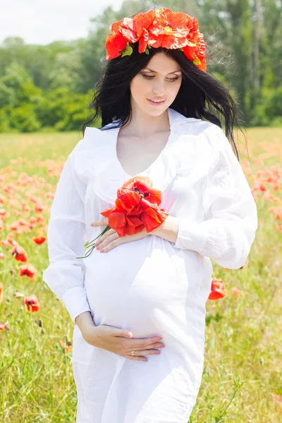 Happy pregnant brunette girl on poppy field — Stock Photo, Image