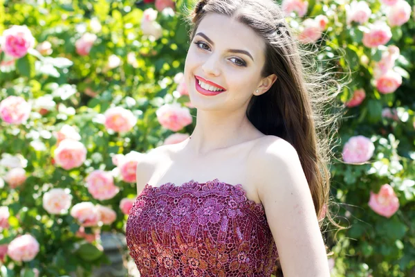 Retrato de cerca de una chica sonriente cerca de rosas rosadas — Foto de Stock