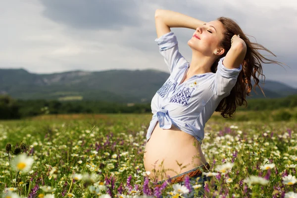 Mulher muito grávida no campo de flores margarida — Fotografia de Stock