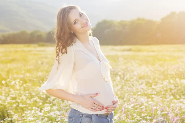 Pregnant woman standing in field behind sunset lights — Stock Photo, Image