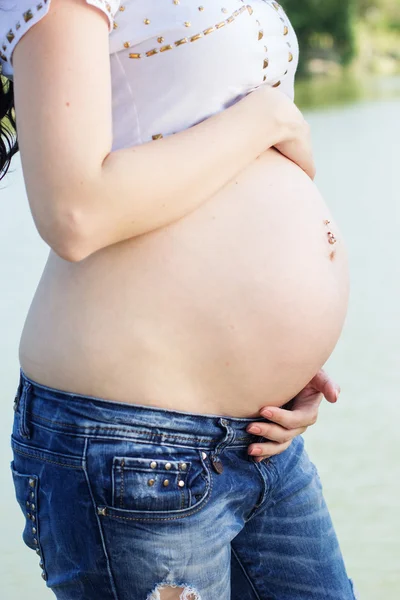 Belly of pregnant girl sitting on bridge near river — Stock Photo, Image