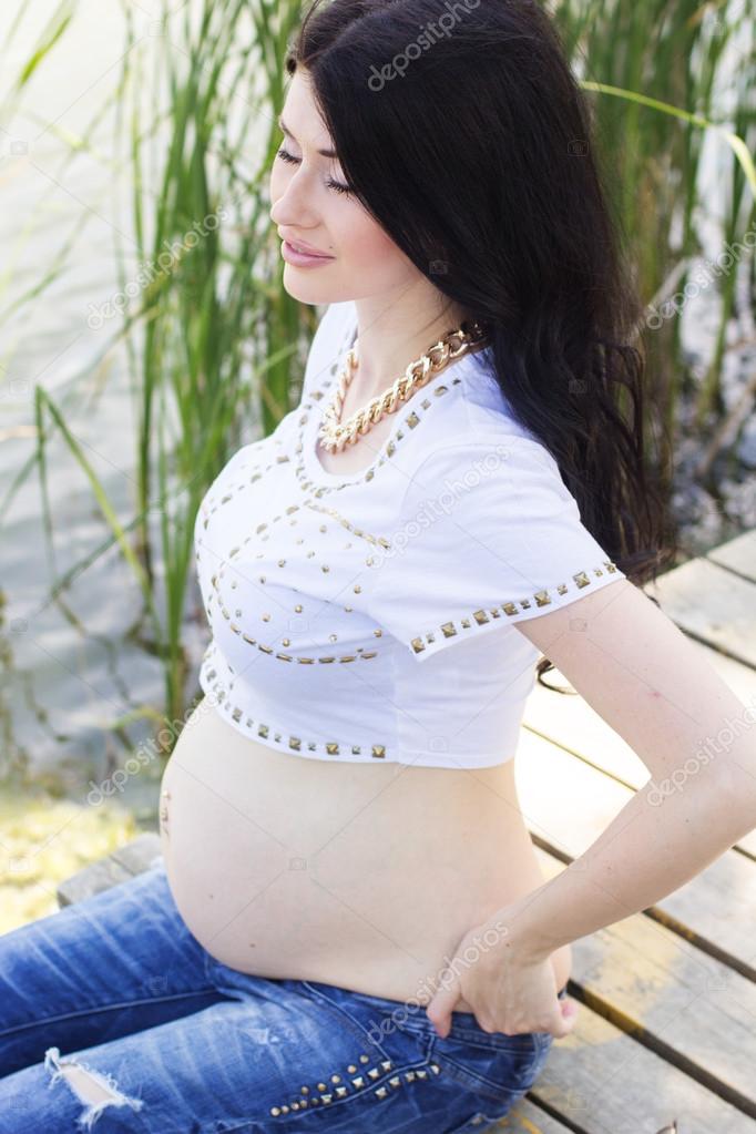 Pregnant pretty woman sitting on bridge near river