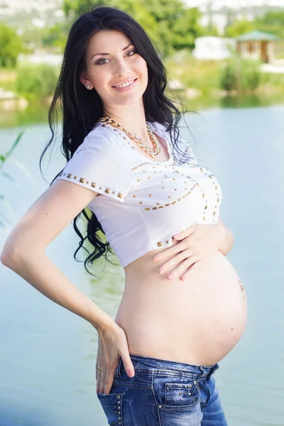 Pregnant girl is standing near blue river — Stock Photo, Image