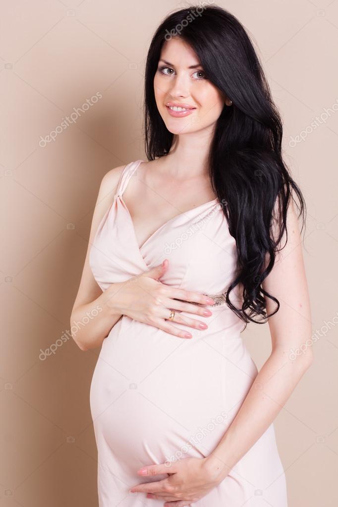 Studio portrait of beautiful pregnant woman holding her belly. 