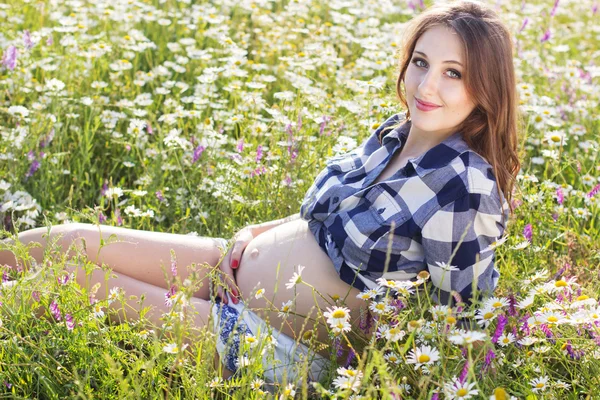 Pregnant smiling woman on field of daisy flowers — Stock Photo, Image