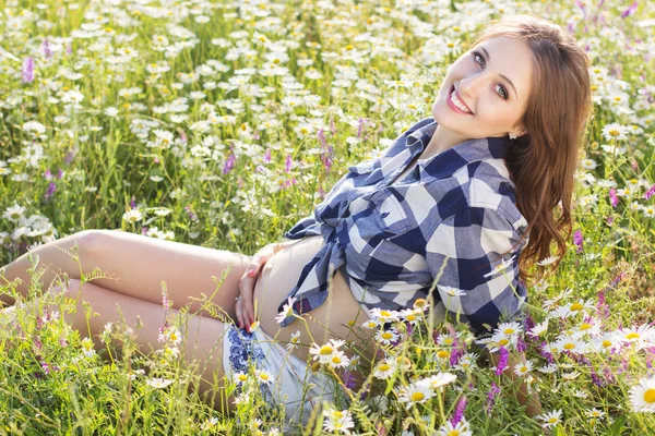 Donna incinta sorridente su campo margherita — Foto Stock