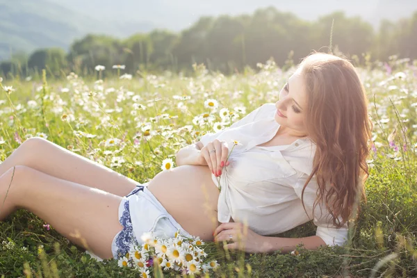 Pregnant woman on daisy field in soft sunset lights — Stock Photo, Image