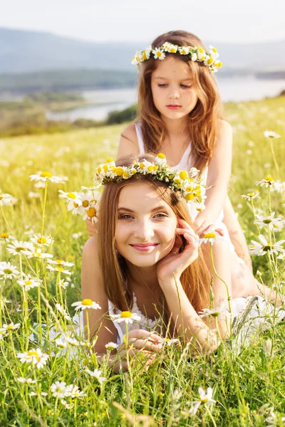 Duas meninas bonitas no prado com vista para a montanha e flores — Fotografia de Stock