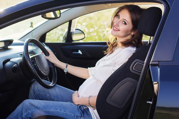 Zwangere gelukkig jonge vrouw zit in zwarte auto — Stockfoto