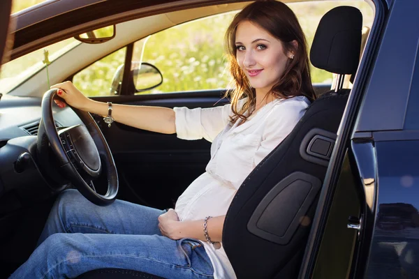 Schwangere glückliche junge Frau sitzt in schwarzem Auto — Stockfoto