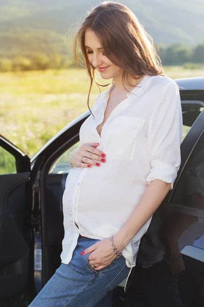 Zwangere gelukkig jonge vrouw in de buurt van auto over de aard — Stockfoto