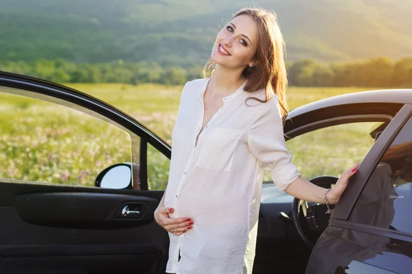 Беременная счастливая молодая женщина возле машины на природе — стоковое фото