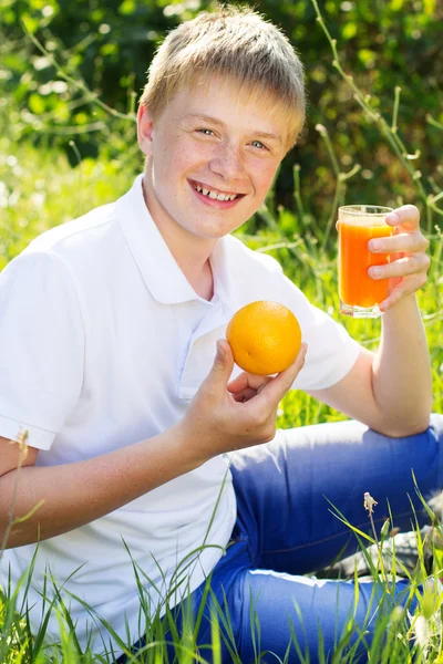 Lindo chico rubio está sosteniendo vidrio con jugo de naranja — Foto de Stock