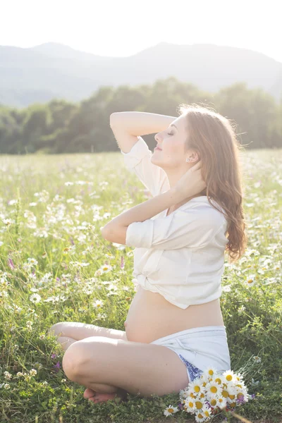 Zwangere lachende vrouw op veld in zonsondergang lichten — Stockfoto