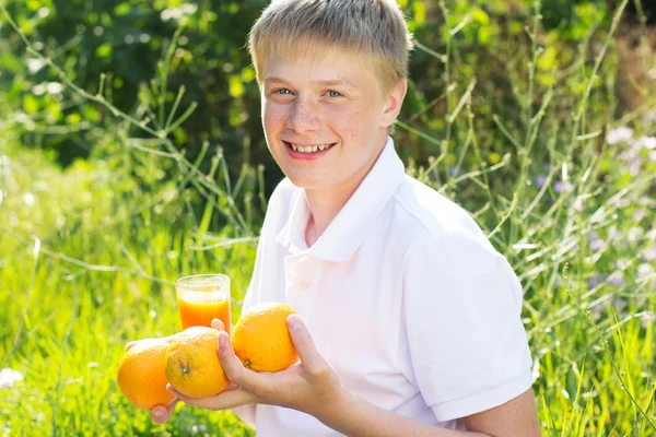 Teenager boy is holding glass with orange juice and fruits — Zdjęcie stockowe