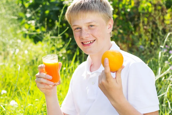 Teenager boy is holding glass with carrot juice and orange — Zdjęcie stockowe